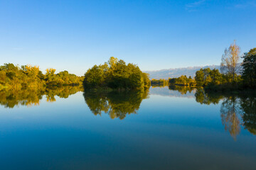 Obraz premium Lake at the edge of the mountains with forest reflected in the clear water. Idyllic autumn landscape. The forest and the sky in the reflection of the water. Quiet autumn fishing landscape