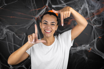 Young beautiful woman over black background with cobwebs and spiders smiling making frame with hands and fingers with happy face