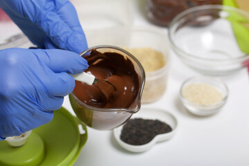 Woman in gloves stirring chocolates for sweets. Cooking candies from dried fruits and nuts at home in self-isolation during an epidemic. The mask and gloves are next to each other.