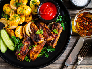 Tasty roasted ribs with baked potatoes vegetables on wooden table
