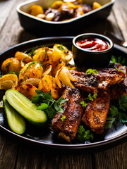 Tasty roasted ribs with baked potatoes vegetables on wooden table
