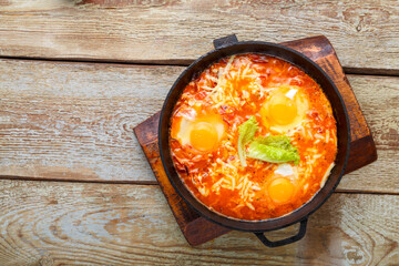 israeli fried eggs shakshuk in a frying pan on a wooden table. copy space