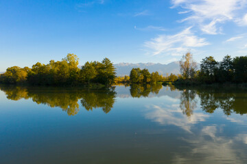Lake at the edge of the mountains with forest reflected in the clear water. Idyllic autumn landscape. The forest and the sky in the reflection of the water. Quiet autumn fishing landscape
