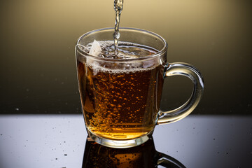 Brew black tea from a sausage bag in a transparent mug with reflection on a gradient background