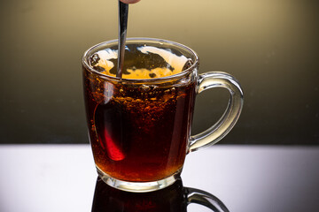 Brew black tea from a sausage bag in a transparent mug with reflection on a gradient background