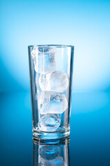 Clear ice water in transparent glass with reflection on blue gradient background