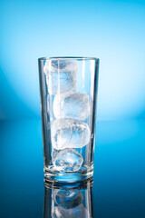 Clear ice water in transparent glass with reflection on blue gradient background