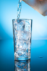Clear ice water in transparent glass with reflection on blue gradient background