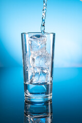 Clear ice water in transparent glass with reflection on blue gradient background