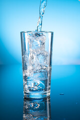 Clear ice water in transparent glass with reflection on blue gradient background