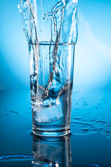 Clear ice water in transparent glass with reflection on blue gradient background