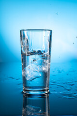 Clear ice water in transparent glass with reflection on blue gradient background