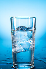 Clear ice water in transparent glass with reflection on blue gradient background