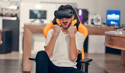 Attractive caucasian bearded man trying virtual reality technology while sitting in chair in tech store.
