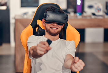 Smiling Caucasian men in white t-shirt  trying out virtual reality technology while sitting in the chair in tech store.