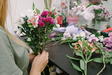 Fototapeta na wymiar Florist at work: pretty young woman making fashion modern bouquet of different flowers.