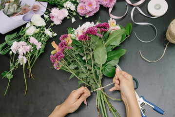 Top view of florist making flower bouquet on wooden surface.Florist at work: pretty young woman making bouquet of flowers.