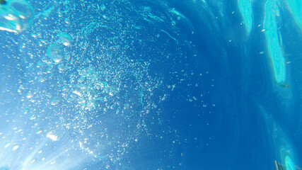 Underwater bubbles emerging to turquoise sea surface