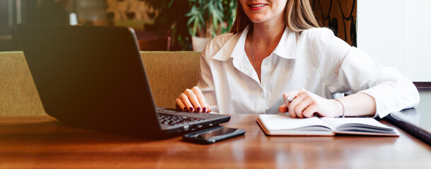 Close up of a female hand writing notes. Female working at a cafe with laptop and mobile phone in front on table. Banner size