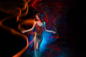 Fototapeta na wymiar Beautiful girl in motion. Colorful mixed light. Young Attractive happy smiling woman in a shiny evening dress is dancing in night club. Black background, long exposure. Active sexy Lady having fun.