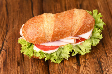 Sandwich with ham and fresh salad on the wooden table.