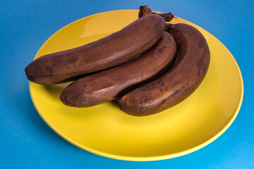 Bunch of ripe yellow-brown bananas on a yellow platter. Close-up.