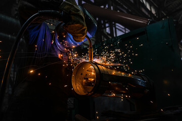 Side view of welder in protective helmet welding metal detail with sparks at factory