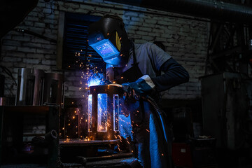 Side view of welder in protective helmet welding metal detail with sparks at factory