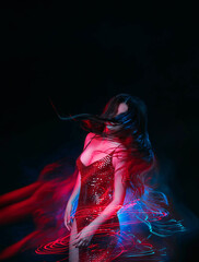 Young beautiful woman in motion. Colorful mixed light. Attractive girl in a shiny evening dress is...