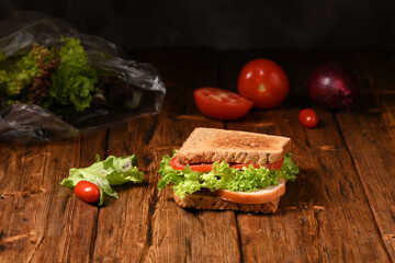 Sandwich with green fresh salad on a wooden table.