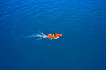 Side view of the speed boat. A large, orange speedboat moving on blue water. Aerial view of fast boat movement. Lonely boat, movement on the water.