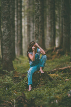young brunette woman combing her hair while sitting on a tree trunk in a pine forest