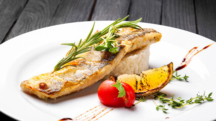 Fried fish with rice on a white plate. Black wooden background.