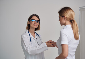 woman doctor in a medical gown shakes hands with a patient in a white t-shirt on a light background