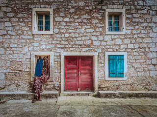 Close up view of old stone house, red wooden door and blue windows. Prvic luka, Summer in Croatia.
