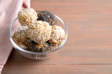 Homemade energy balls made from dried fruits, nuts, granola with sesame, almonds and poppy seeds on a brown wooden background. Vegan food. Close-up, copy space