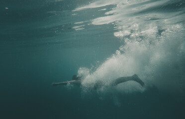 Fototapeta premium European young woman diving and jumoing underwater in Croatia in mediterranean sea with a big splash and water bubbles
