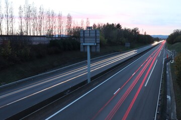 Trainées de lumières de phares de voitures au coucher du soleil sur le boulevard urbain sud de Lyon, ville de Corbas, département du Rhône, France