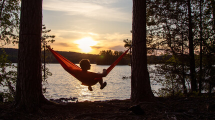 Person in Hängematte am See bei Sonnenuntergang
