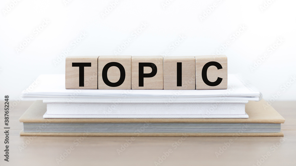 Poster topic written with wooden cubes on a stack of books on the table.
