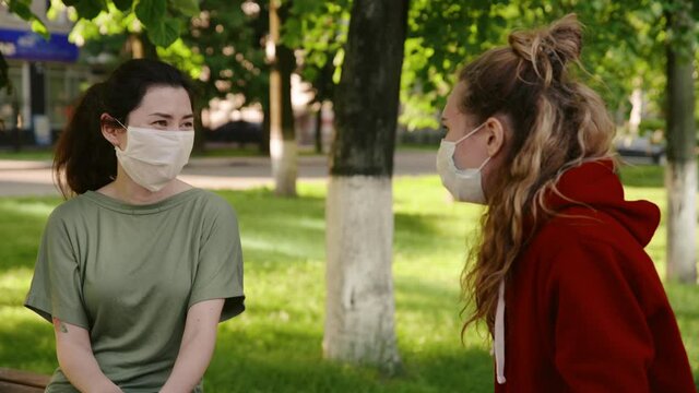 Young pretty girls talk to each other in protective masks from the coronovirus and laughting. Woman tells her friend a funny story. New life after covid-19 epidemic. Concept of pandemic, corona.