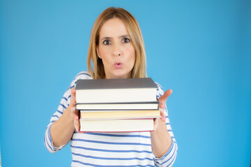 Isolated young happy beautiful woman holding books over blue background.