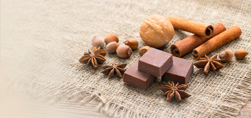 Pieces of chocolate, cinnamon sticks, walnuts and star anise stars. Confectionery shop advertising and culinary ingredients concept, copy space, mock up for recipe