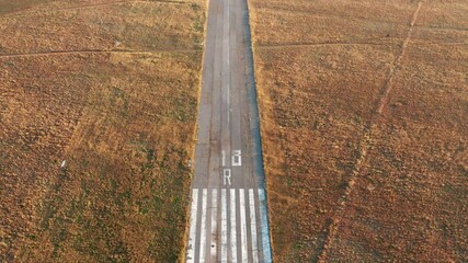 Empty runway of a small airport used for takeoff and landing of light aircraft. Airfield for general aviation and light-sport planes in the middle of a field covered with yellow grass.