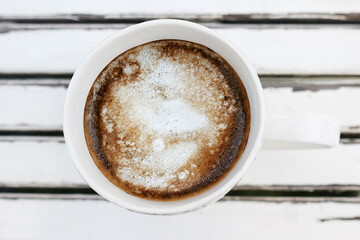 White ceramic cup of coffee on white wooden background outdoors, top view.