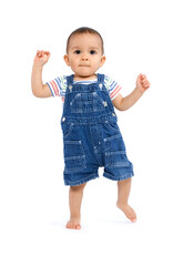 A baby boy learning to walk, dressed in overalls and isolated on white background