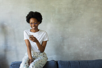 Happy african American young woman sit relax on cozy couch happy to move to new apartment. Smiling black girl rest on comfortable sofa in living room dreaming
