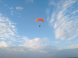 A skydiver with a bright orange sports parachute wing flies before landing in the summer against a blue sky background close up