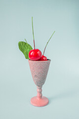 Creative food decoration concept made with cherry fruits in pink elegant glass on blue pastel background