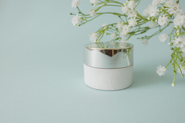 Herbal  organic natural dermatology cosmetic hygienic cream with flowers skincare product in glass jar on  pastel blue background 